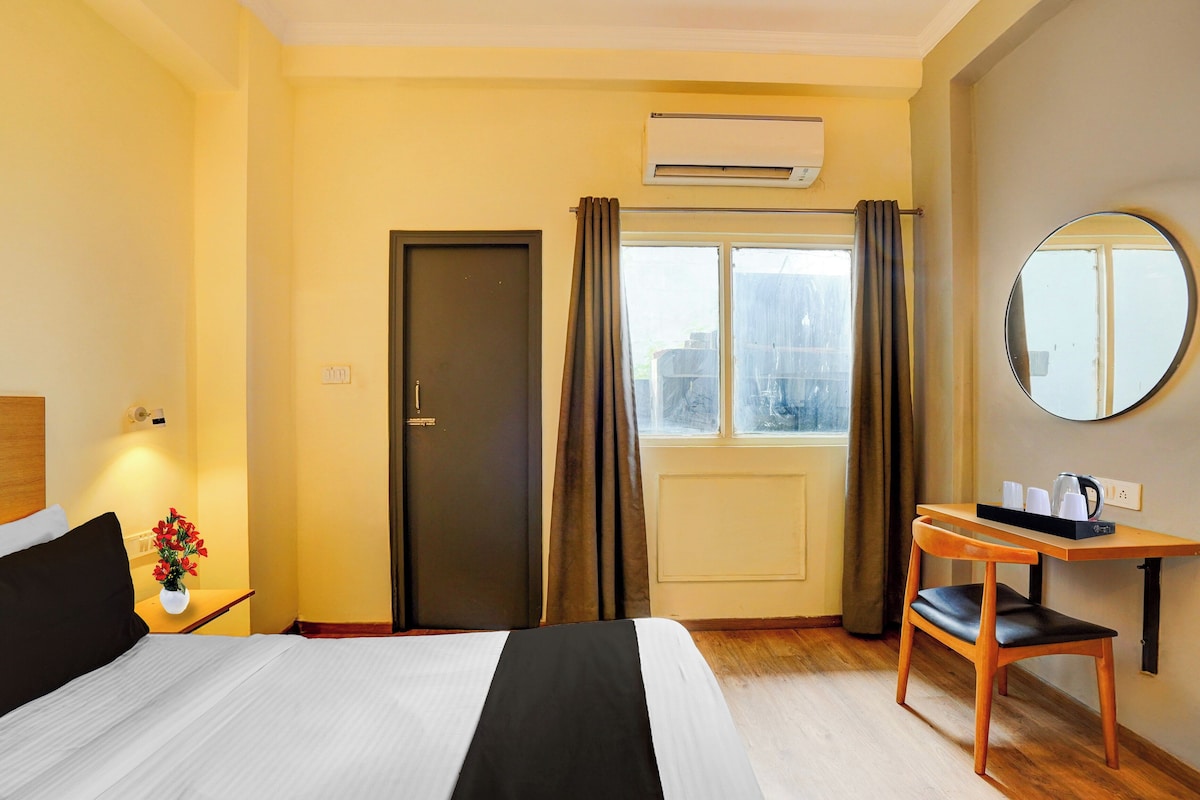 A hotel room with a bed, a desk with a chair, a mirror, and a window with curtains.