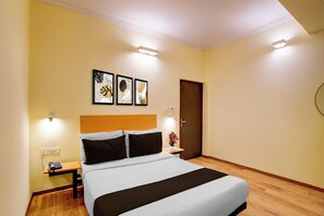 Una habitació d'hotel amb un llit, taules de nit, una tauleta al costat del llit, una làmpada penjada a la paret i una porta.