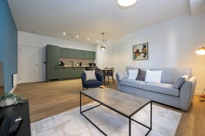 Ein modernes Wohnzimmer mit einem grauen Sofa, einem Couchtisch und einer Küche im Hintergrund.
