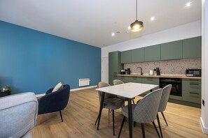 Eine moderne Küche mit grünen Schränken, einer weißen Arbeitsplatte und einem Essbereich mit Tisch und Stühlen.
