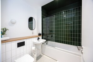 Ein modernes Badezimmer mit einem weißen Waschbecken, einem Spiegel, einer Toilette und einer Dusche mit schwarzen Fliesen.