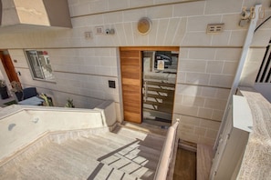 A modern hotel interior with a staircase leading to a wooden door, a view of a parking garage, and a tiled wall. - Spacious 2 Bed 2 Bath Apartment in Swieqi (Swieqi)
