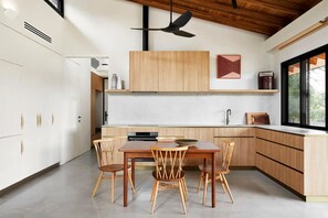 A modern kitchen with wooden cabinets, a dining table with chairs, and a ceiling fan. - Ukiyo House - 2 Bedroom “The Floating World” (Port Willunga)