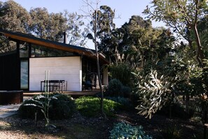 A modern house with a large glass window, a wooden deck, and a garden with various plants. - Ukiyo House - 2 Bedroom “The Floating World” (Port Willunga)