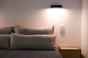 A bed with multiple pillows and a bedside table with a light switch. - Ukiyo House - 2 Bedroom “The Floating World” (Port Willunga)