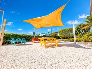 A beachside area with picnic tables and a large yellow shade sail. - Renovated Lagoon View Condo with Pool in San Pedro (San Pedro)