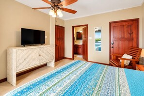 A bedroom with a bed, a TV on a wooden cabinet, a ceiling fan, and a view of a beach through a door. - Renovated Lagoon View Condo with Pool in San Pedro (San Pedro)