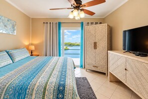 A hotel room with a bed, a television, a wardrobe, a ceiling fan, and a view of the outdoors. - Renovated Lagoon View Condo with Pool in San Pedro (San Pedro)