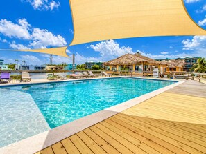 A clear blue pool with wooden deck and lounge chairs, surrounded by buildings with thatched roofs. - Renovated Lagoon View Condo with Pool in San Pedro (San Pedro)