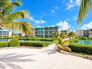 A resort with a pool, palm trees, and a building with multiple balconies. - Renovated Lagoon View Condo with Pool in San Pedro (San Pedro)