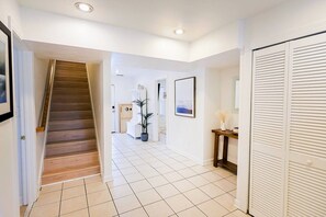 A hallway with a wooden staircase, white tiled flooring, a potted plant, and a closed white closet. - 9BR Ocean Estate • Pool • Hot Tub, 350 FT to Beach (Virginia Beach)