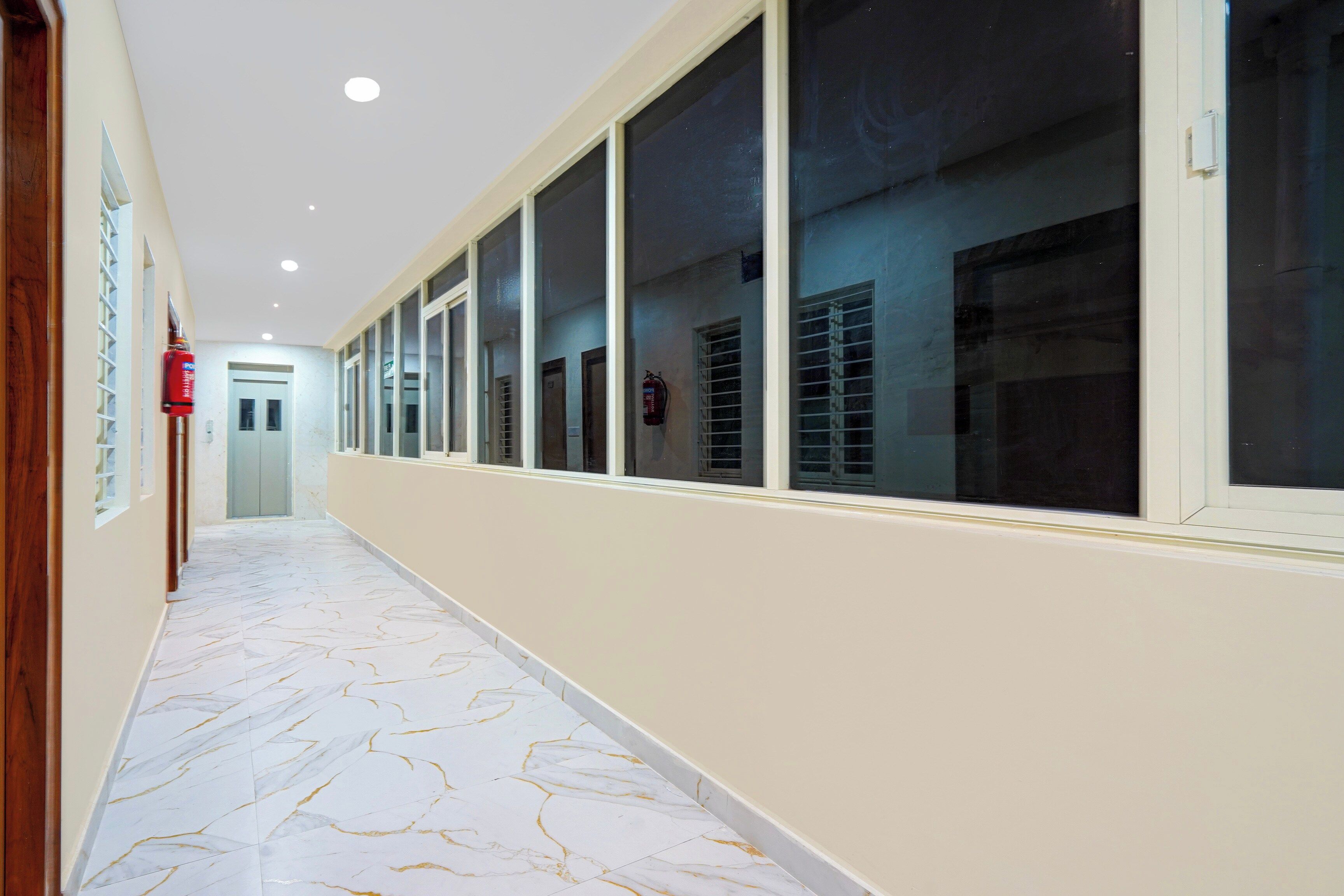 A corridor with a marble floor, large windows, and a fire extinguisher on the wall.
