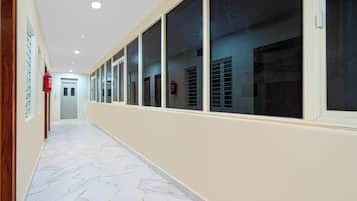 A corridor with a marble floor, large windows, and a fire extinguisher on the wall.