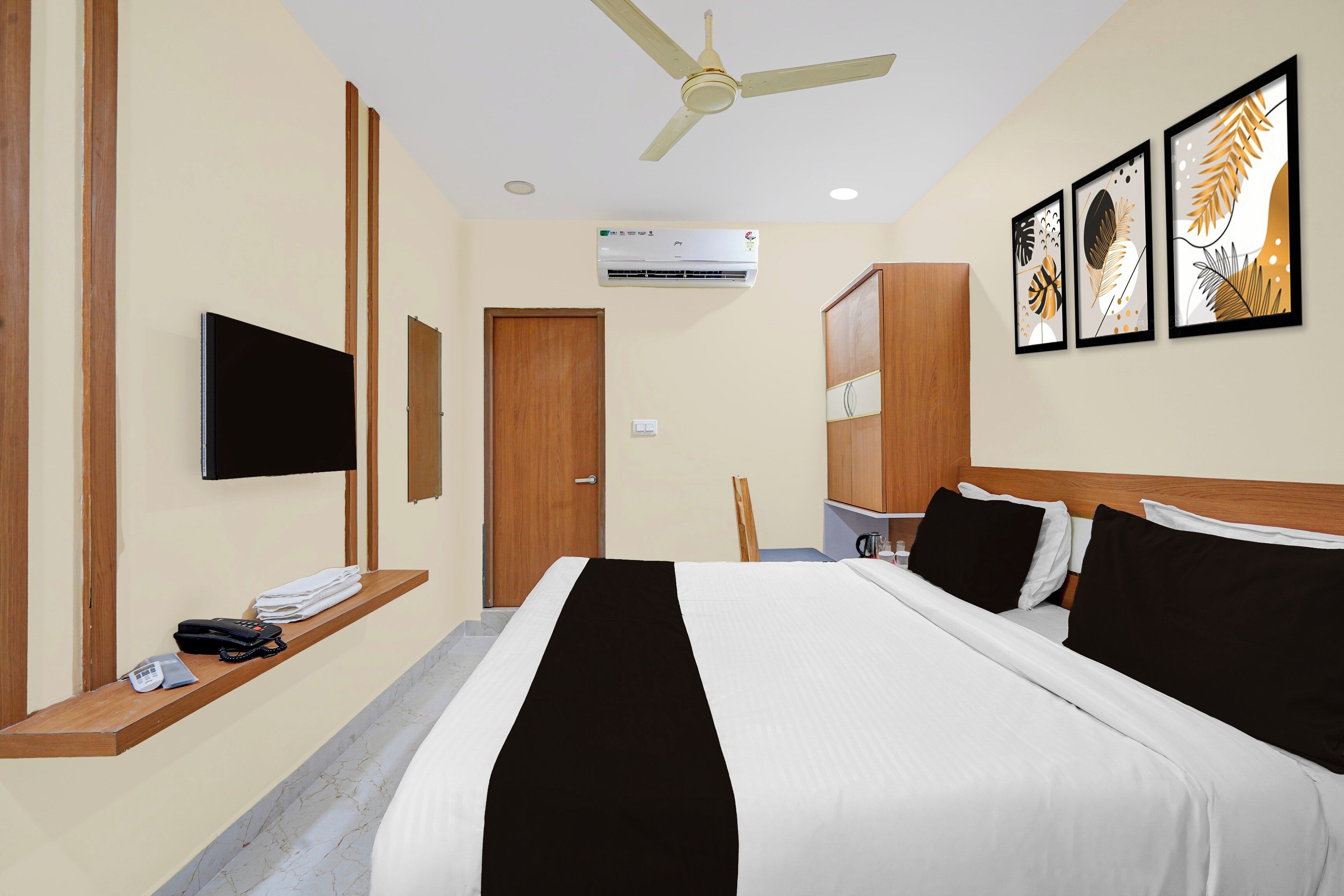 A hotel room with a bed, a flat-screen TV, an air conditioning unit, and artwork on the wall.