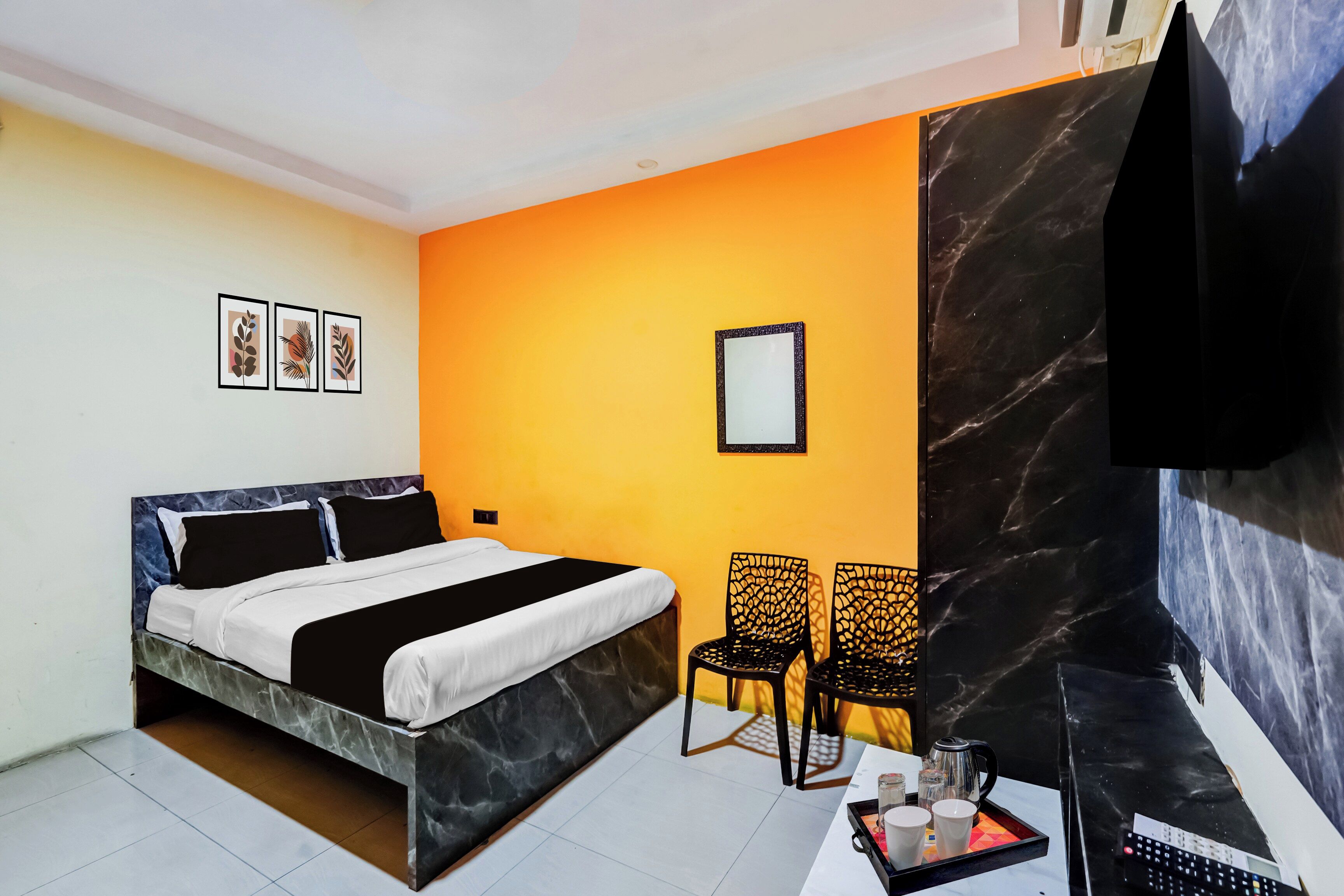 A hotel room with a bed, two chairs, a table with a tray of items, and a TV.