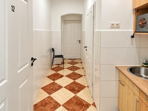A hallway with a checkered floor, a door at the end, and a kitchen area with a sink and cabinets. - Unpack in Vienna 1BR for Longer Stays (Wien)