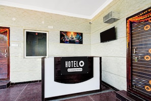 A hotel reception desk with a sign indicating it is company-serviced. There is a framed picture above the desk and a door with a decorative floral design to the right. - Super Hotel O Square Mall Hyderabad (Hyderabad)