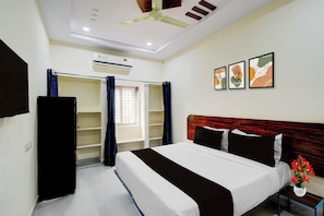 A hotel room with a bed, a nightstand, a window with curtains, a ceiling fan, and wall art. - Super Hotel O Square Mall Hyderabad (Hyderabad)