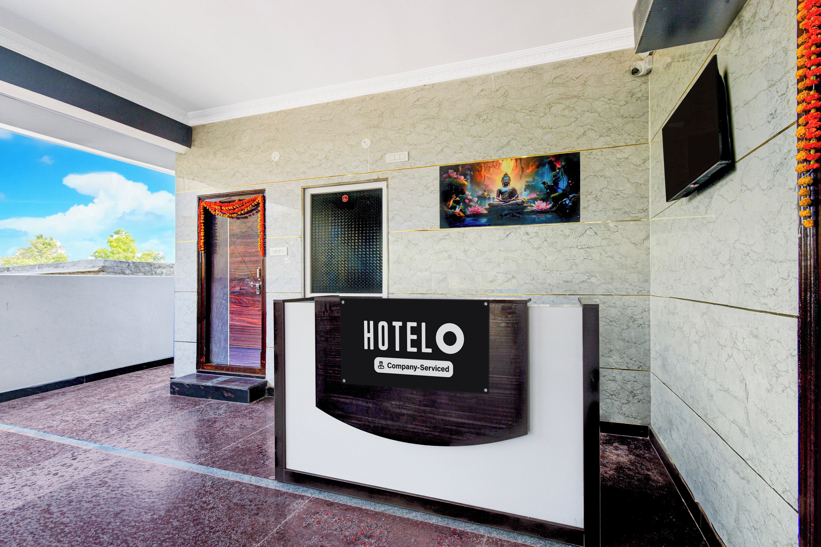 Een hotel receptie met een receptiebalie, een aan de muur bevestigde televisie en een ingelijst schilderij erboven.