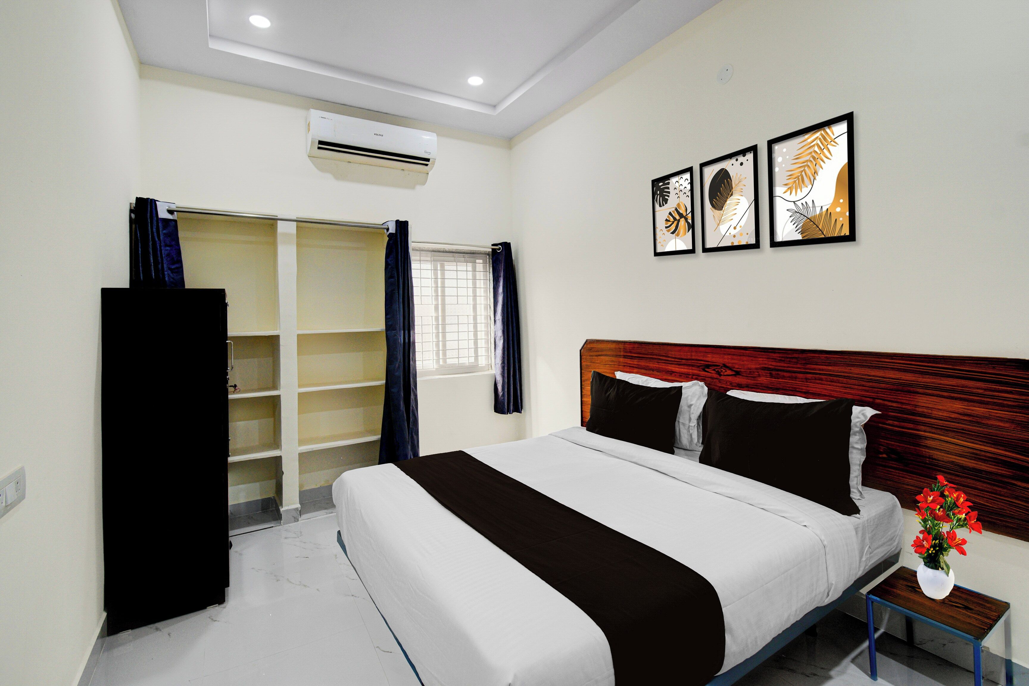 A hotel room with a bed, a wardrobe, a small table with a vase, and a window with curtains.