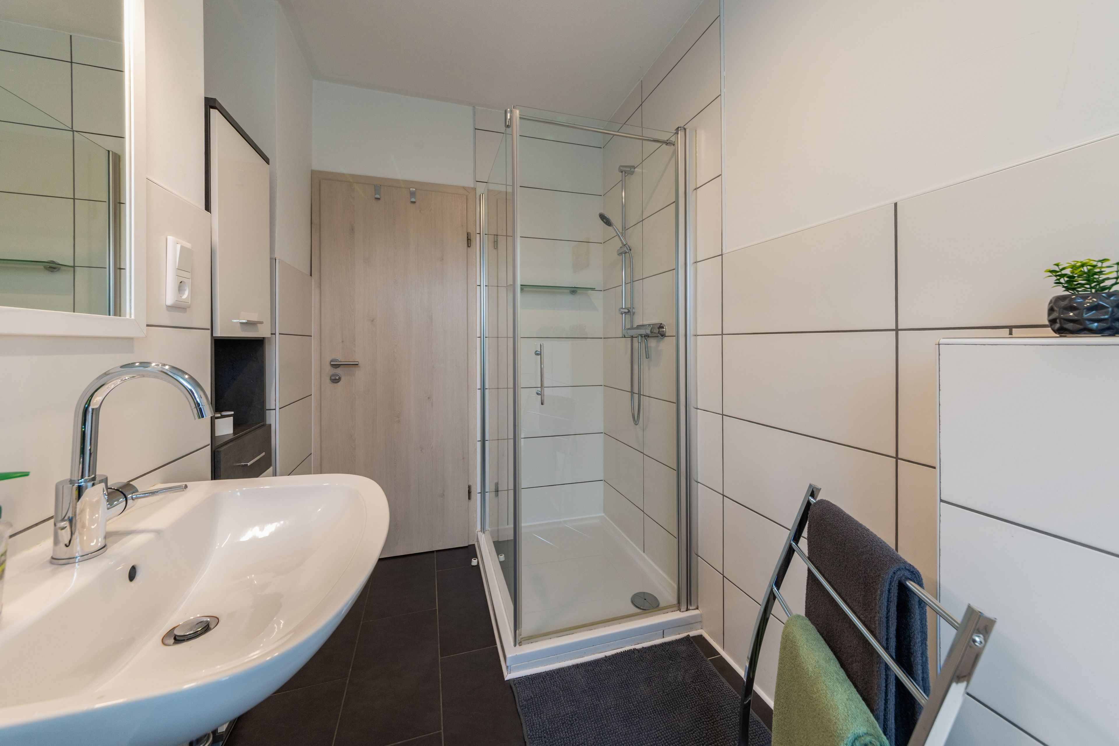 A bathroom with a white sink, a glass shower enclosure, and a towel rack with towels.