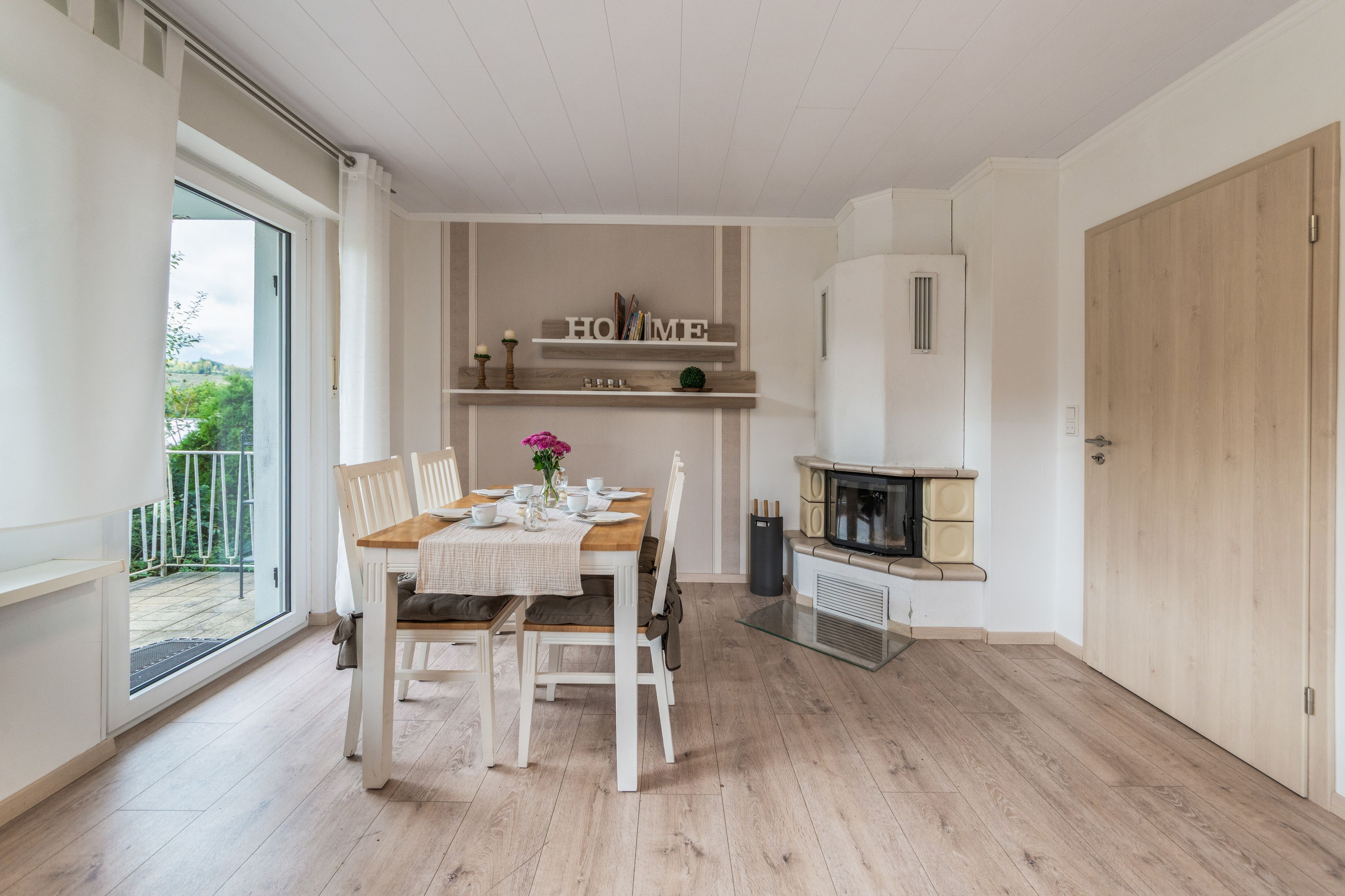 Ein Essbereich mit einem für vier Personen gedeckten Tisch, einem Kamin und Blick durch eine Glastür auf einen Balkon.