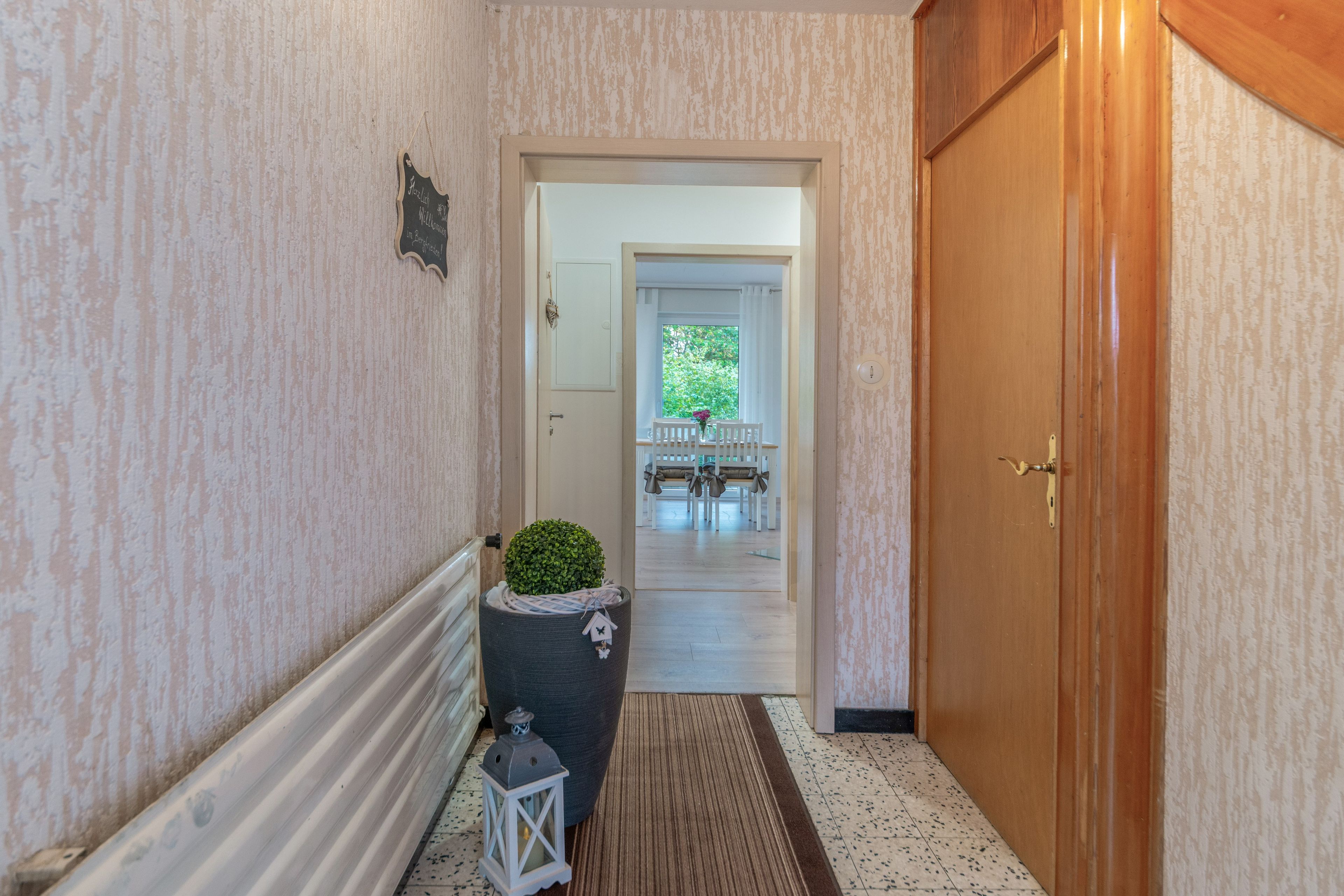 Ein Flur mit einer Holztür, einem Blumentopf und einem kleinen Tisch mit Stühlen.