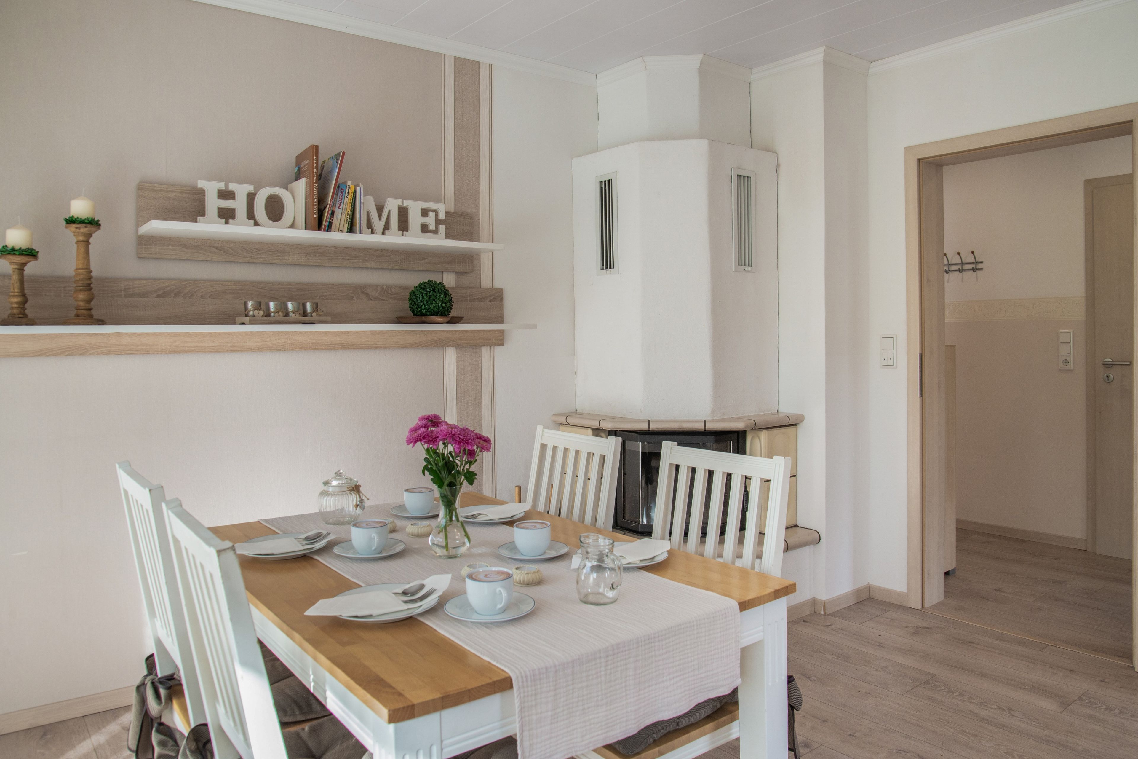 A dining area with a table set for four, a white cabinet with 'HOME' on the top shelf, and a small potted plant on the lower shelf.