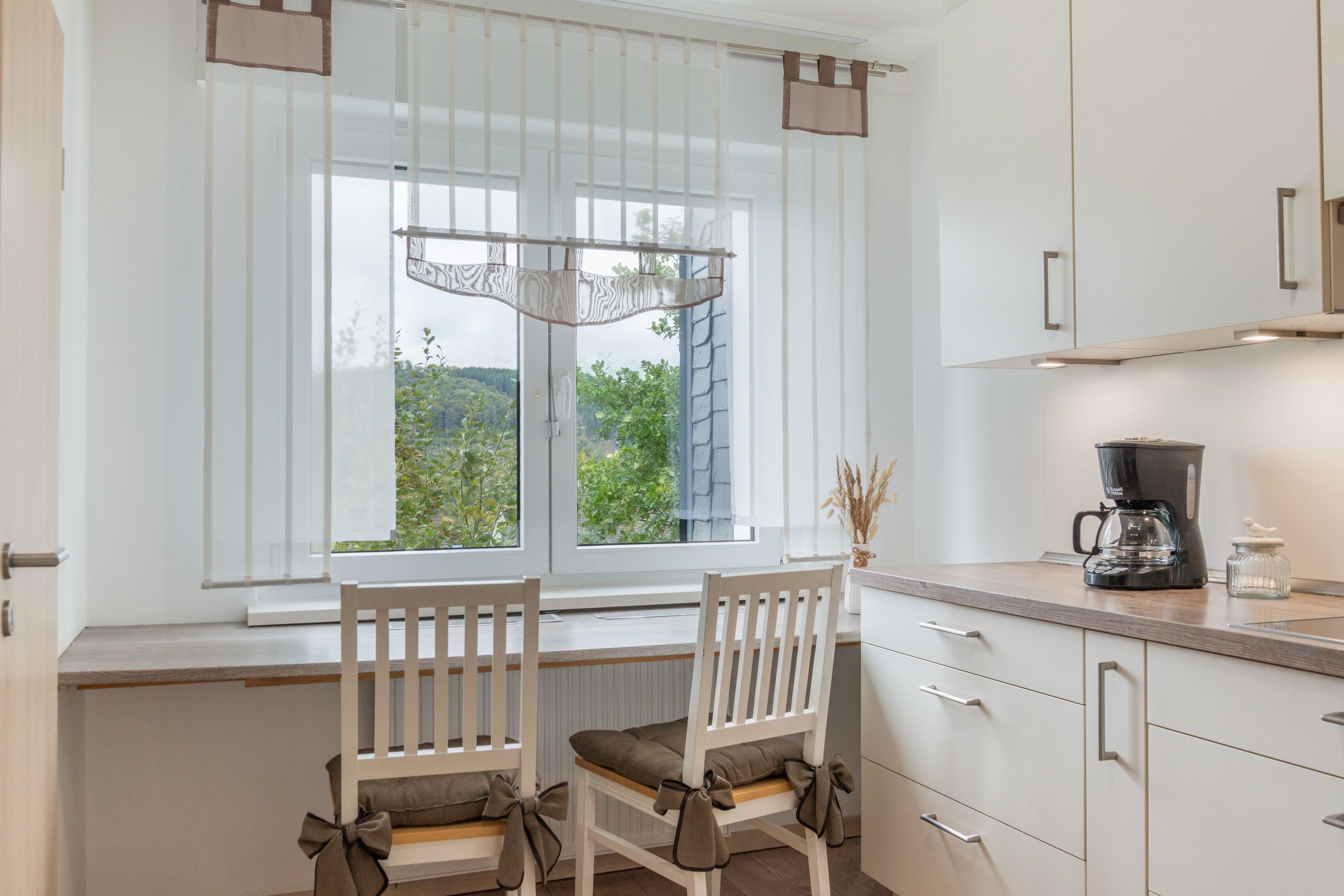 Eine Küche mit zwei Holzkufen, einem Fenster mit Blick auf Grünflächen und einer Kaffeemaschine auf der Arbeitsplatte.