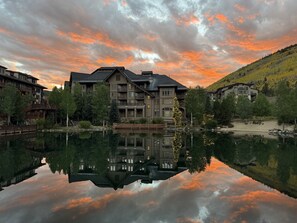 Ein mehrstöckiges Hotel mit Spiegelung in einem ruhigen See, umgeben von Bäumen und einer hügeligen Landschaft.