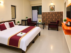 A hotel room with a bed, two chairs, a small table, a TV, and a kitchenette area.