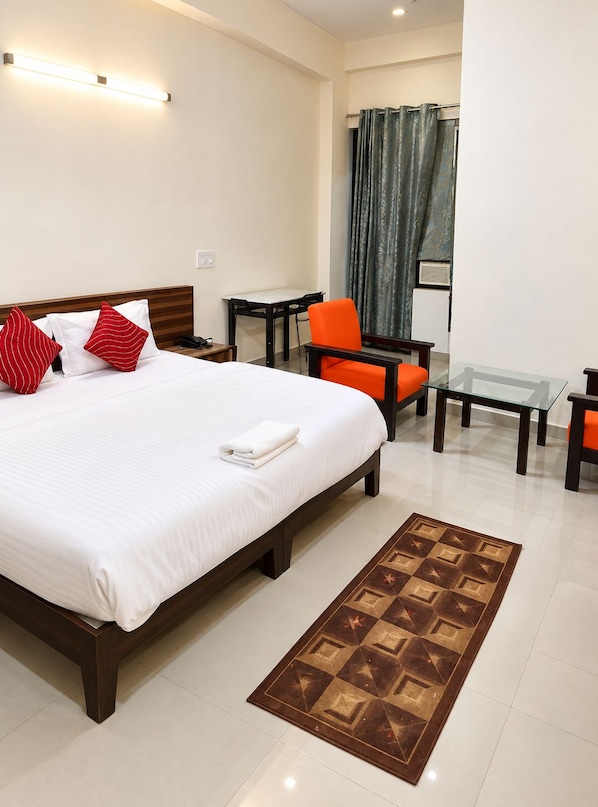 A hotel room with a large bed, a desk, an orange chair, and a glass coffee table.