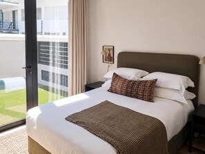 Ein Hotelzimmer mit einem großen Bett, Blick ins Freie, einem Nachttisch mit Lampe und einem gerahmten Bild an der Wand.