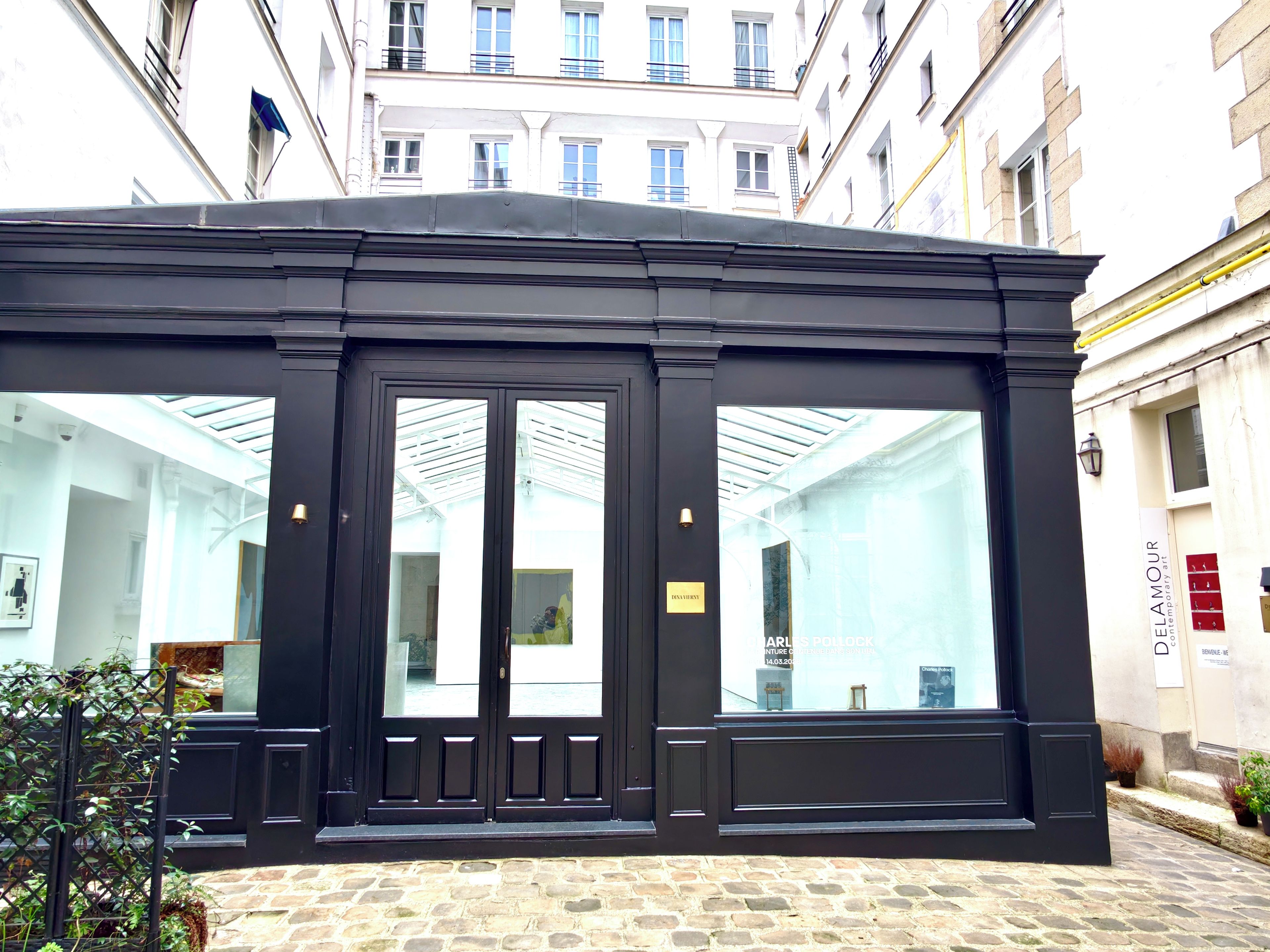 A black-framed entrance with glass doors, a bell, and a sign indicating a gallery or exhibition space.