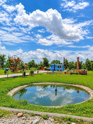Un parque con un estanque, área de juegos y un tren azul.