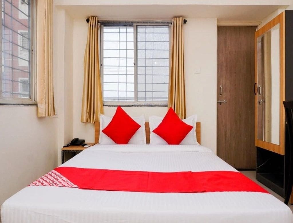 Une chambre d’hôtel avec un lit, des rideaux, une fenêtre, une armoire et un bureau avec un téléphone.