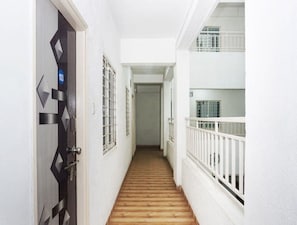 Un pasillo estrecho con piso de madera, paredes blancas y una puerta con diseño geométrico.