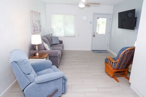 A living room with a sofa, a blue armchair, a wooden rocking chair, a lamp, and a television mounted on the wall. - East Shore Resort. 1 Bedroom apt, full kitchen, living room, screened in porch. (Clearwater)