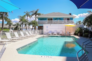 A swimming pool with lounge chairs and umbrellas, a building with a balcony, and palm trees. - East Shore Resort. 1 Bedroom apt, full kitchen, living room, screened in porch. (Clearwater)