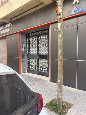 Une devanture de magasin avec une grille métallique, un arbre devant et une voiture garée à proximité.