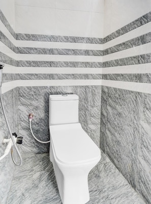 Un baño con inodoro blanco, paredes con diseño de mármol y zona de ducha con manguera.