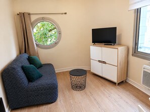 Una habitación con sofá, televisor sobre un mueble de madera, ventana redonda y una pequeña mesa redonda.