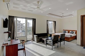A hotel room with a bed, a desk with a chair, a sofa, and a TV. - Townhouse Merriment Near ISKCON Temple (Noida)
