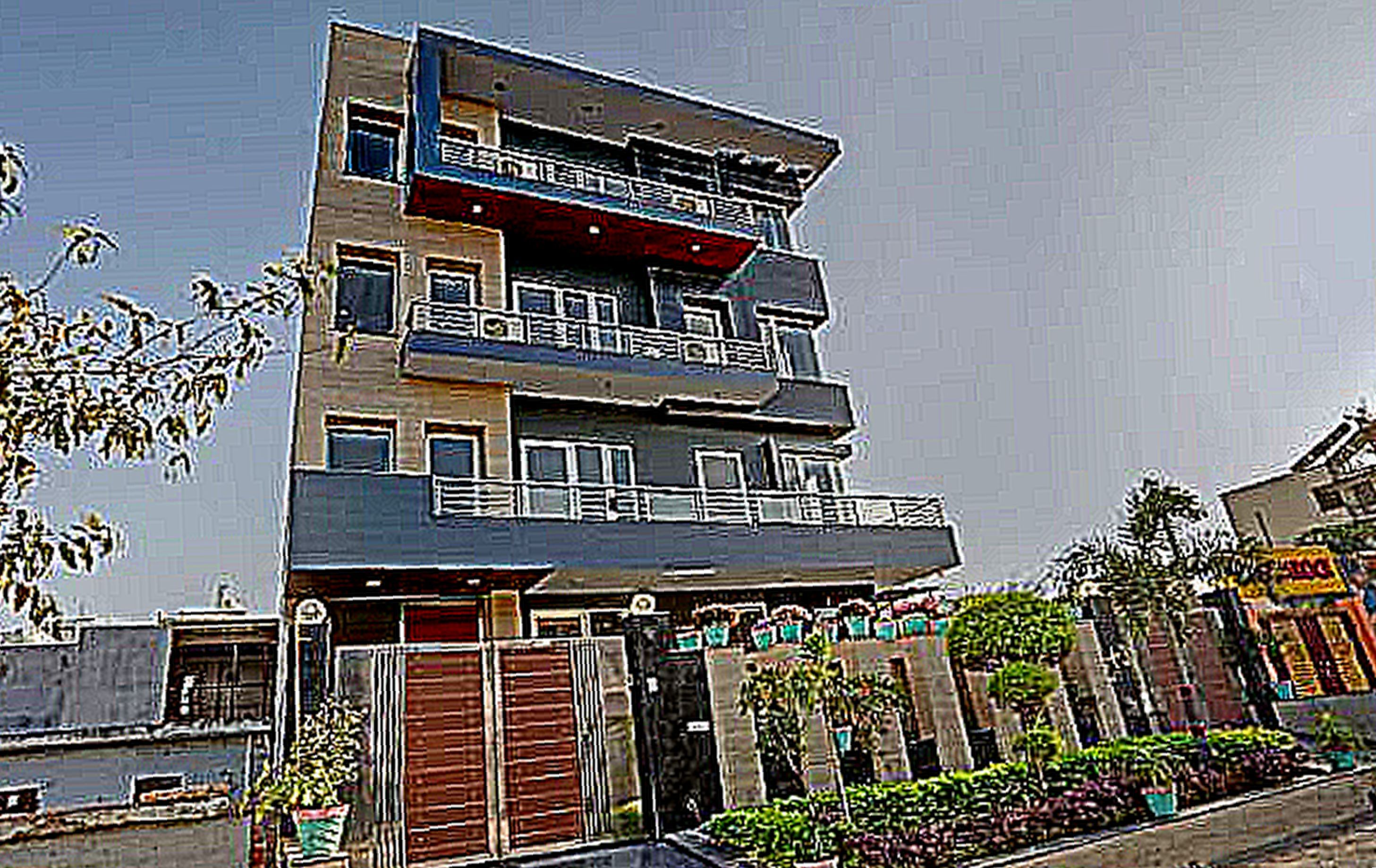 A multi-story building with balconies, a gated entrance, and a landscaped area with plants.