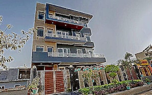 A multi-story building with balconies, a gated entrance, and a landscaped area with plants. - Townhouse Merriment Near ISKCON Temple (Noida)