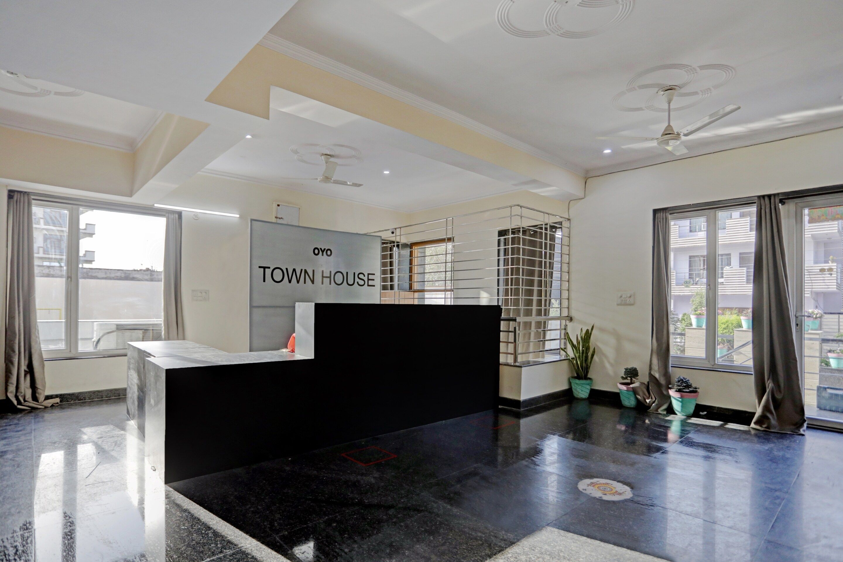 A reception area with a black reception desk, a sign that reads 'OYO TOWN HOUSE', and a view of the outside through large windows.