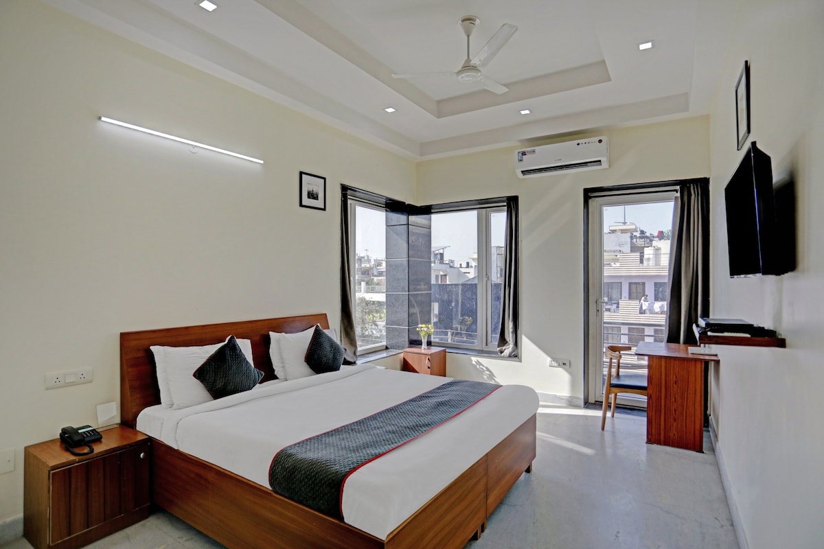 A modern hotel room with a large bed, bedside table, a desk with a chair, a ceiling fan, and a TV mounted on the wall.