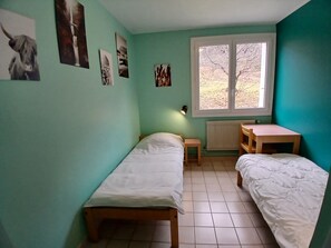 Una habitació amb dos llits individuals, una taula petita, un radiador i una finestra amb vista.