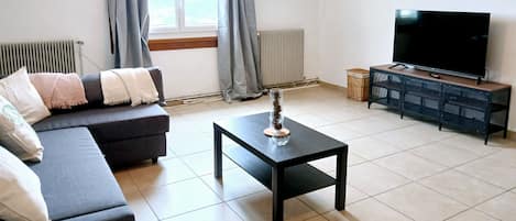 Ein Wohnzimmer mit einer Couch, einem Couchtisch, einem Fernseher und einem Fenster mit Vorhängen.