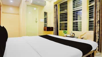 Una habitación de hotel con una cama, una ventana con persianas, una silla y una mesita con una planta y una tetera.